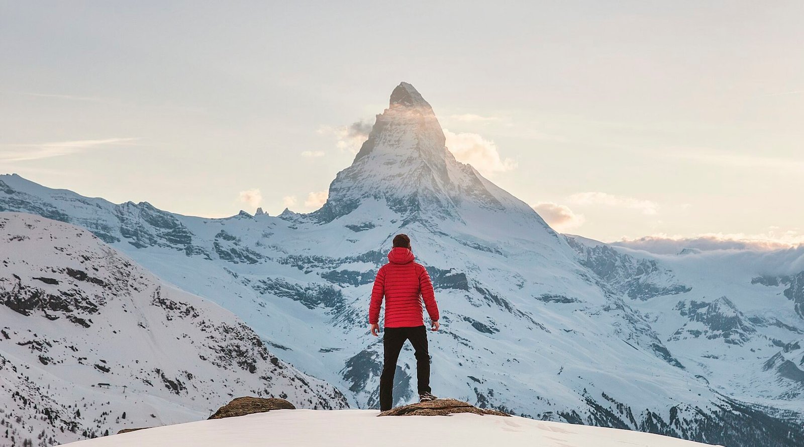 Hiker in a red jacket looking at a snowy mountain peak