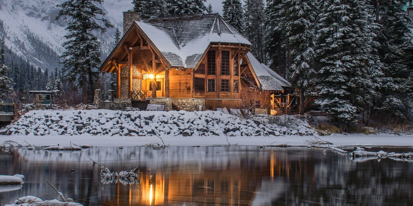 Cozy lakeside vacation cabin surrounded by snowy pine forest at dusk