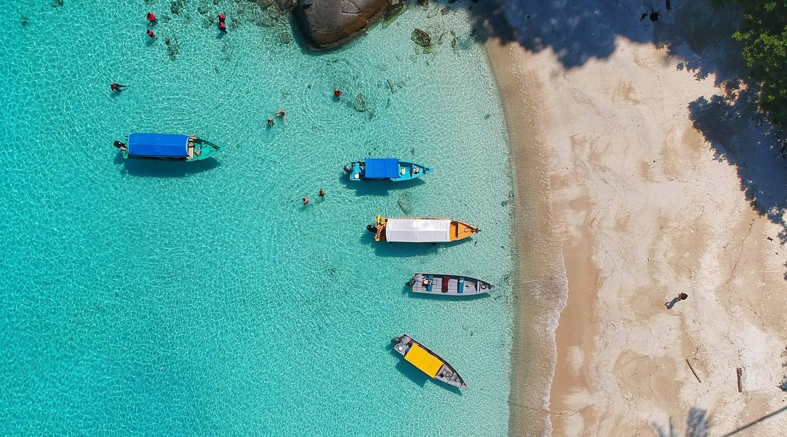 Island-hopping boats in turquoise water near a white-sand beach